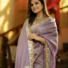 Portrait of a woman smiling in a premium purple net saree with intricate mirror work and embroidery.