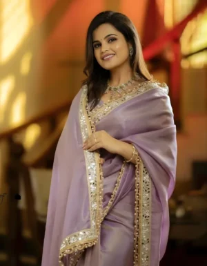 Portrait of a woman smiling in a premium purple net saree with intricate mirror work and embroidery.