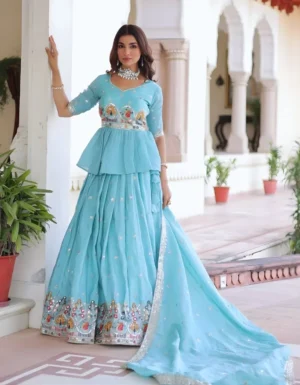 "Full-length view of turquoise lehenga set with peplum blouse, tiered skirt with multi-colored embroidered border, flowing dupatta, and pearl jewelry on colonial architecture background"