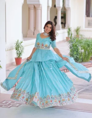 "Woman in turquoise lehenga with peplum blouse positioned against white marble column with green landscape, wearing coordinating dupatta and traditional jewelry for festive occasion"