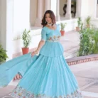 "Woman wearing sky blue lehenga choli with multi-thread gold embroidery, zari detailing, and sequins, paired with ornate choker necklace against palatial marble backdrop"